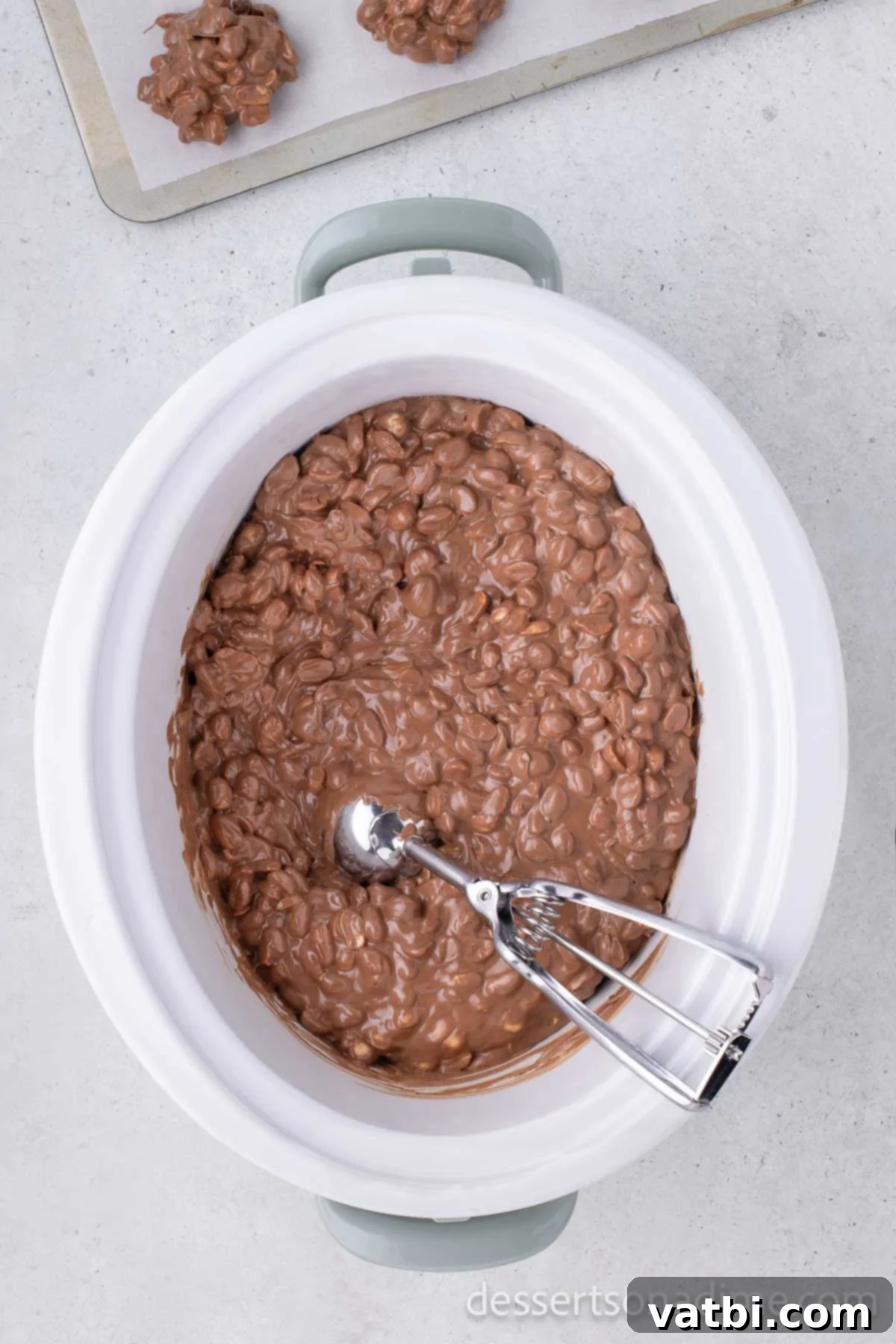 Crock pot with mixture and a cookie scoop inside.