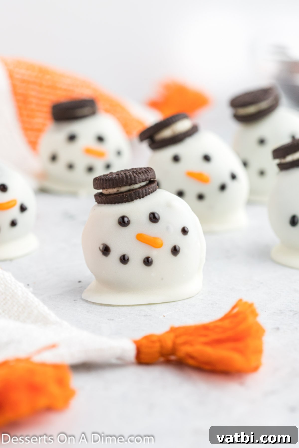 Whimsical Winter Oreo Bites 2 Snowman oreo balls grouped together, some with mini Oreo hats, decorated with orange carrot noses and black icing eyes/mouths.