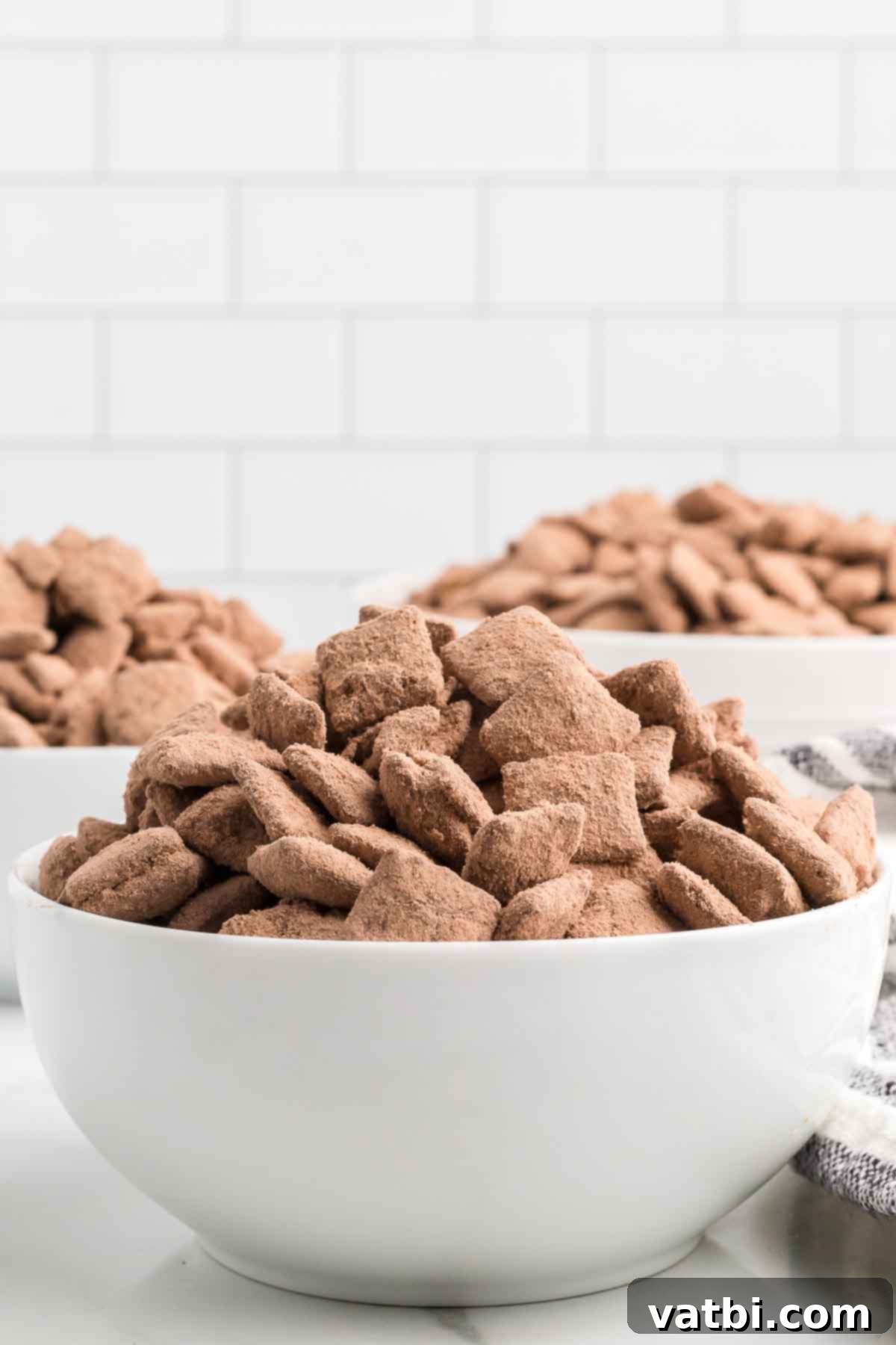 Decadent Brownie Muddy Buddies 2 A large bowl filled with delicious brownie puppy chow, ready to be served. The pieces are coated in a rich chocolate and brownie mix.