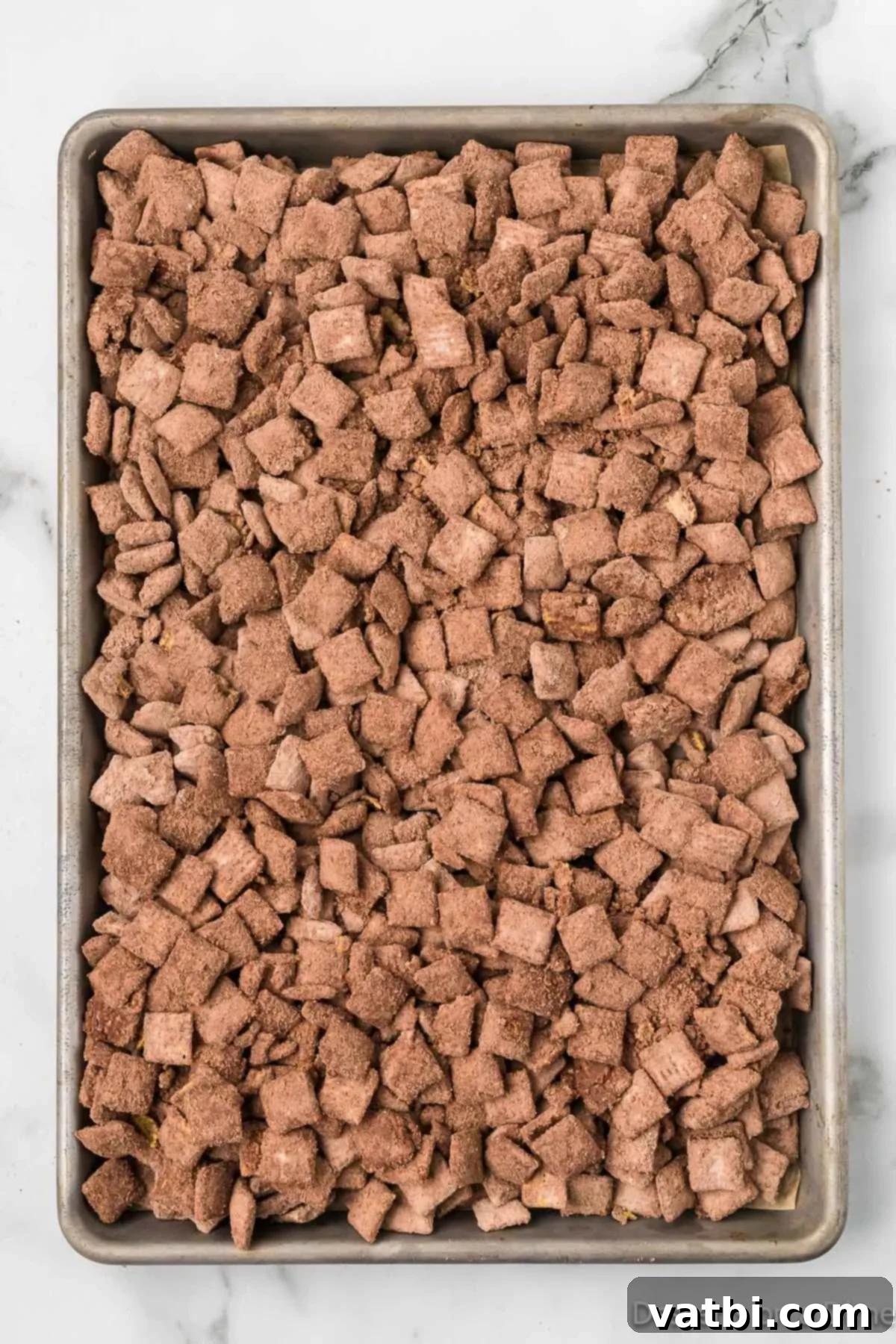 Decadent Brownie Muddy Buddies 10 Brownie puppy chow spread out in a single layer on a parchment-lined baking sheet to cool.