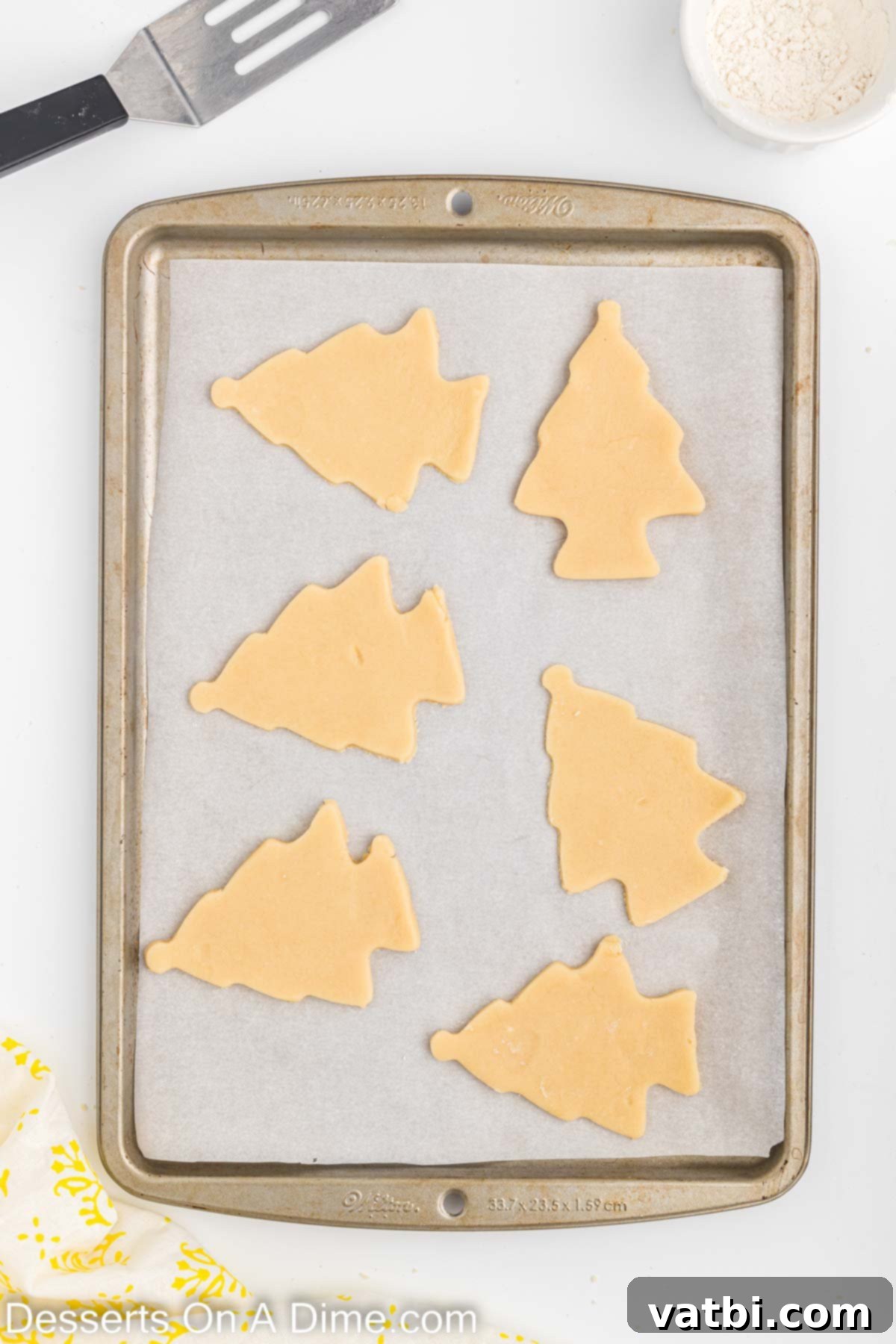 Festive Christmas Tree Sugar Cookies 6 A baking sheet neatly lined with parchment paper, showcasing multiple Christmas tree shaped cookie dough cutouts, perfectly arranged and ready for the oven.