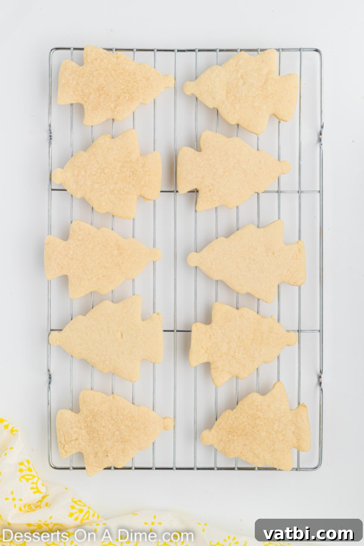 Festive Christmas Tree Sugar Cookies 7 Freshly baked Christmas Tree Sugar Cookies, with lightly browned edges, cooling gracefully on a wire rack to ensure they reach perfect room temperature before frosting.
