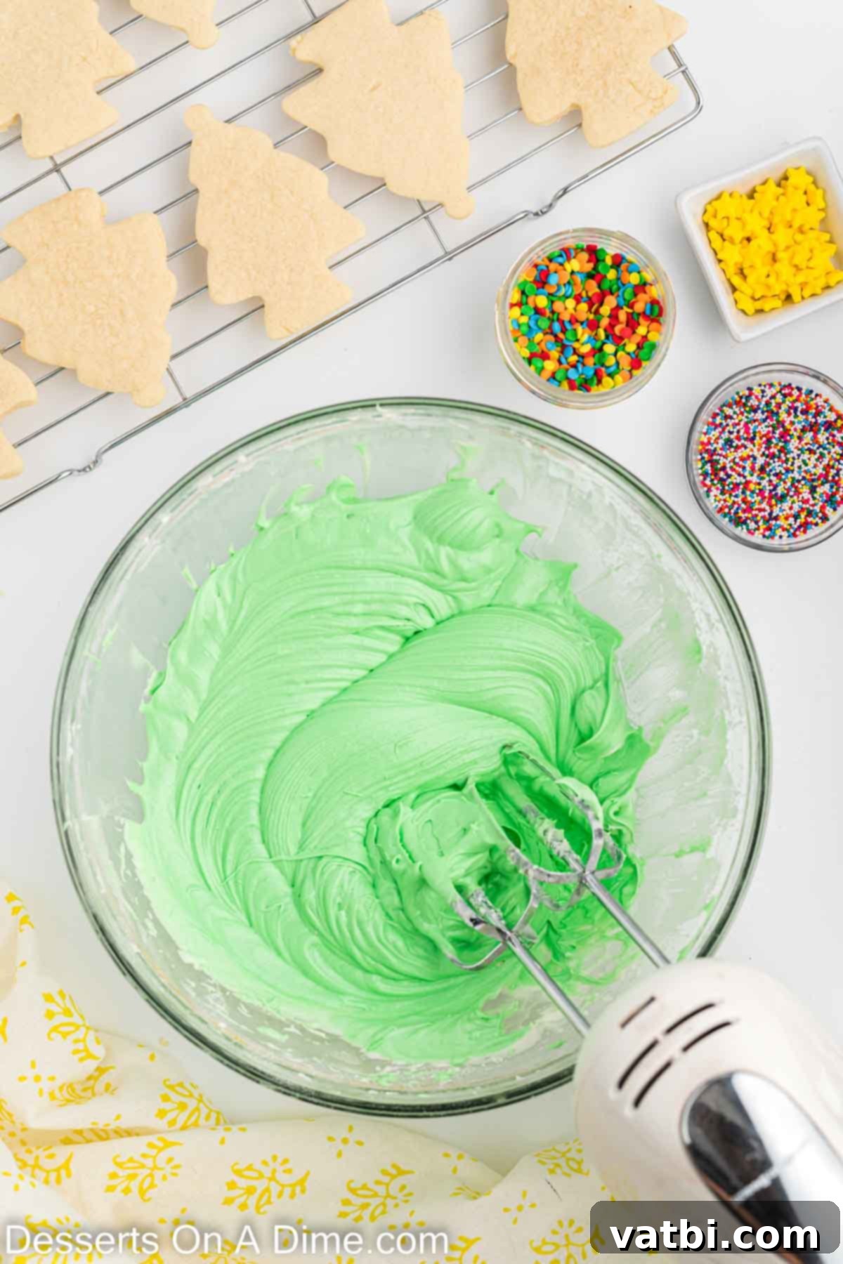 Festive Christmas Tree Sugar Cookies 10 Green gel food coloring being expertly mixed into the smooth cream cheese frosting, gradually transforming it into a vibrant and festive Christmas green hue.