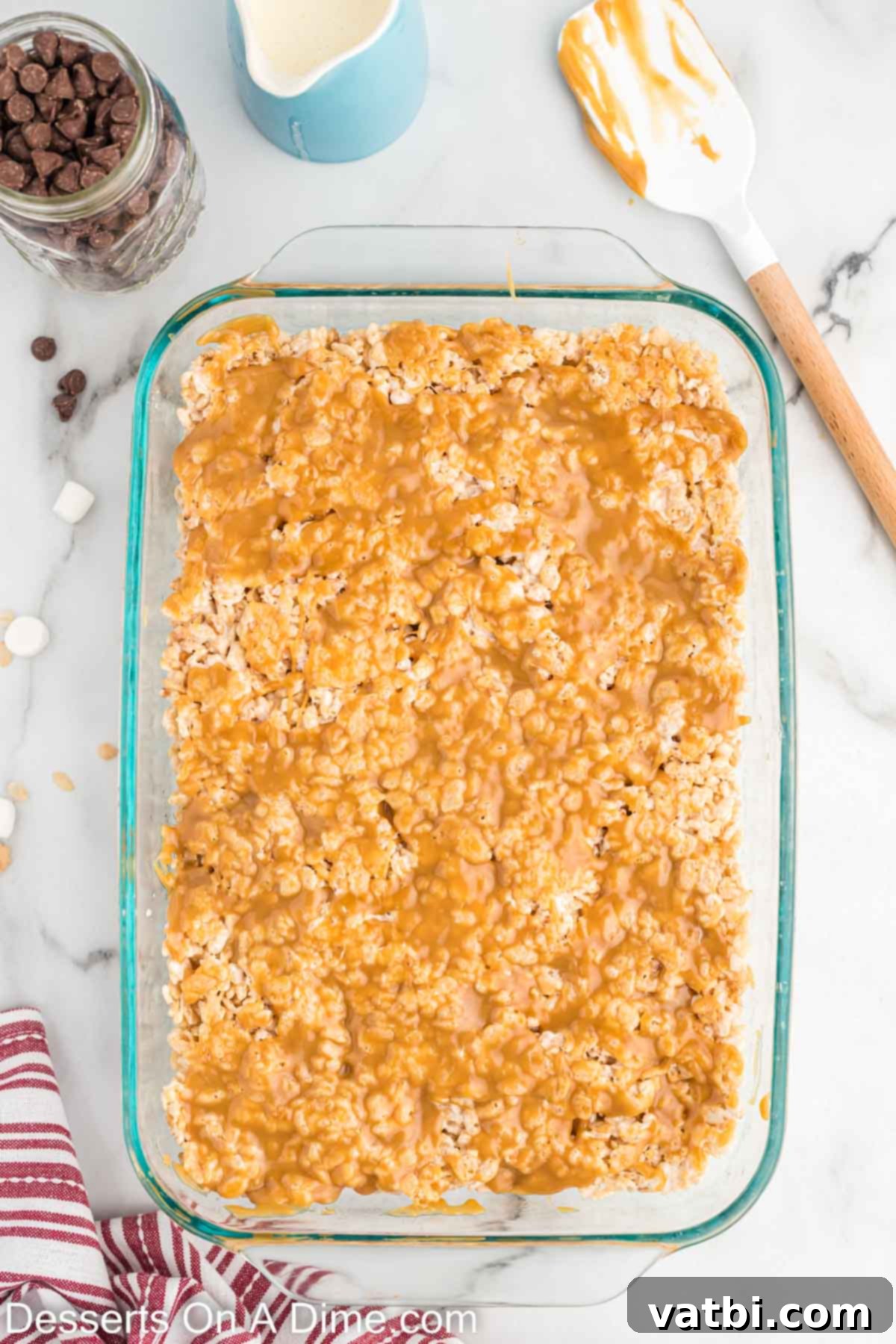 Warm salted caramel sauce being carefully spread over the chilled Rice Krispie treats in the baking pan.