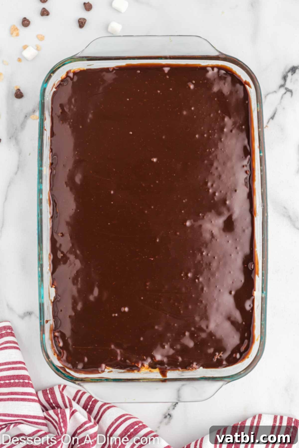 Smooth chocolate ganache being poured and spread over the set caramel and Rice Krispie layers in the pan.