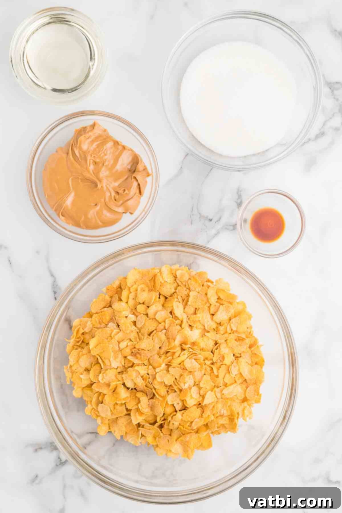 Fresh cornflake cereal, granulated sugar, light corn syrup, creamy peanut butter, and pure vanilla extract laid out for making no-bake cornflake cookies.