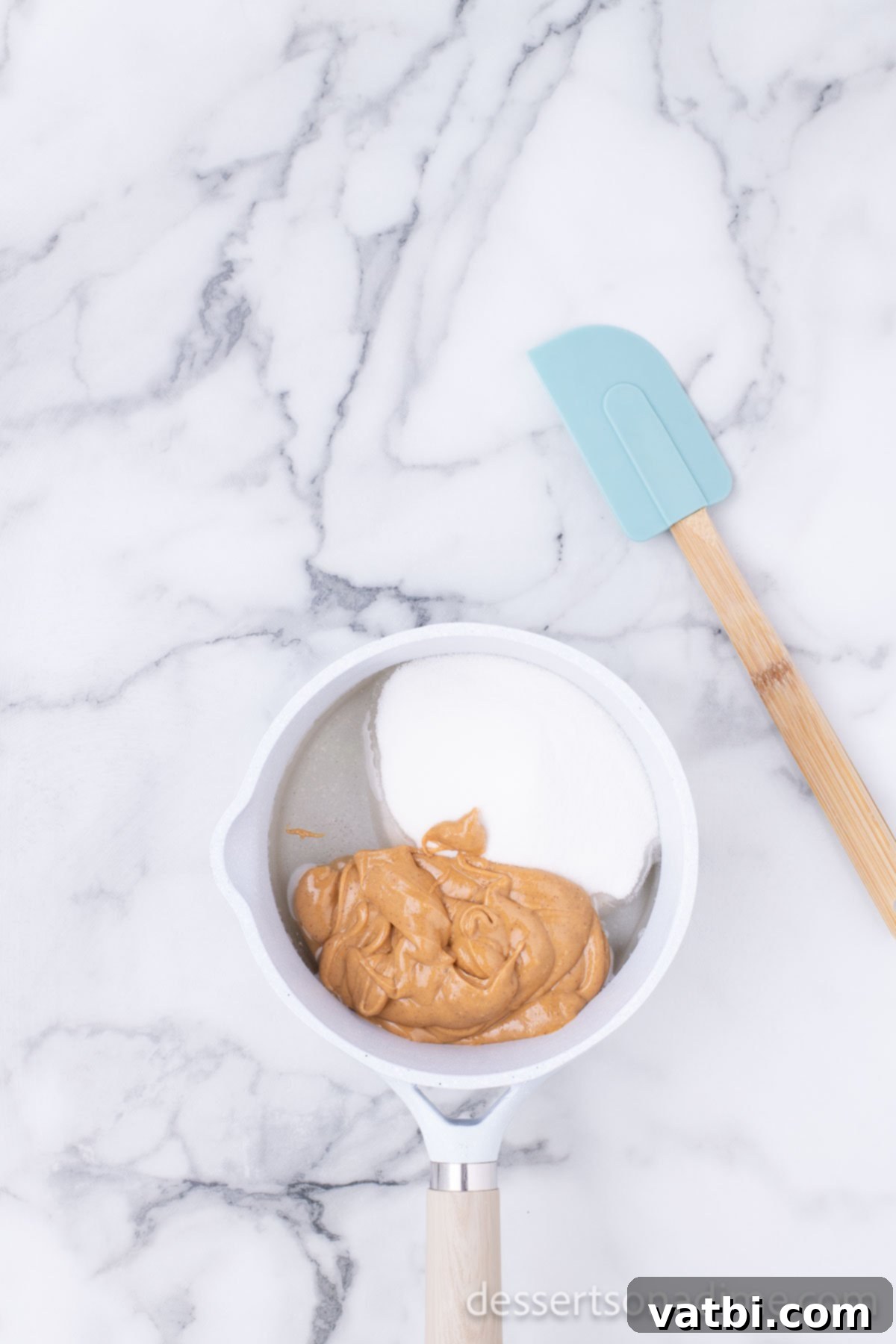 Creamy peanut butter being stirred into the simmering sugar and corn syrup mixture in a saucepan.