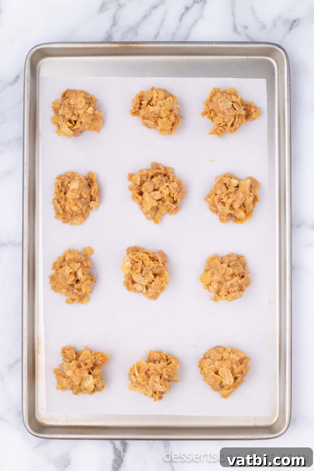 Scoops of no-bake cornflake cookies being neatly placed on a baking sheet lined with parchment paper to set.