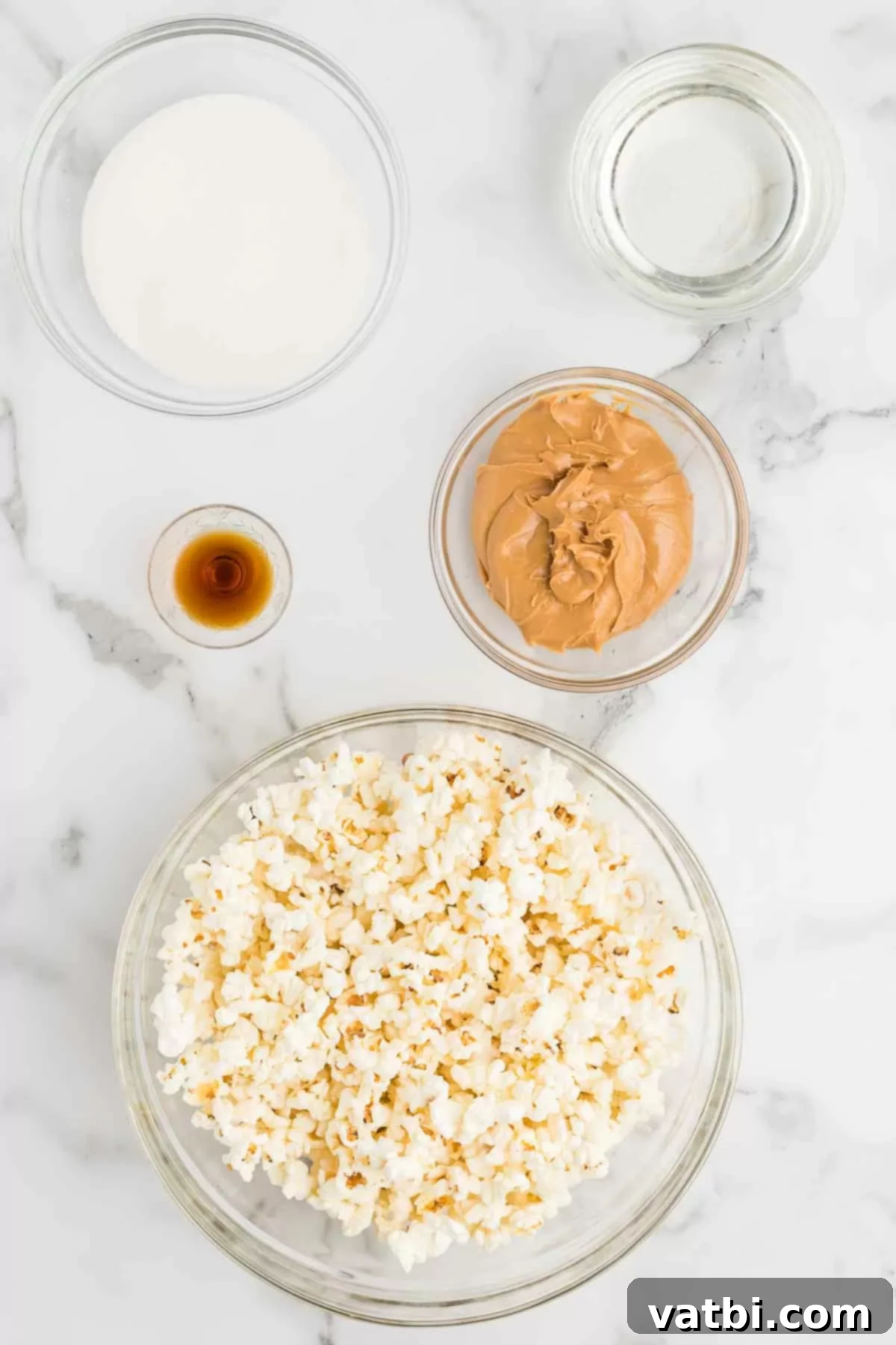 Collection of ingredients for peanut butter popcorn, including popped popcorn, creamy peanut butter, vanilla extract, corn syrup, and granulated sugar.