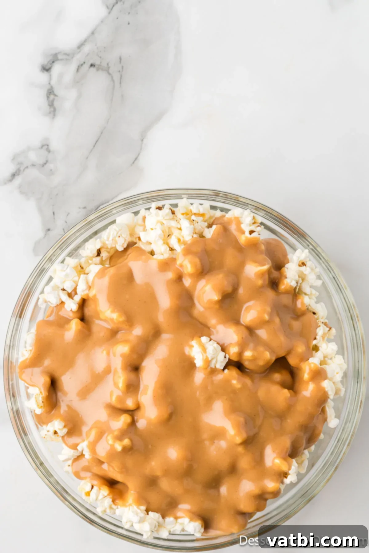 Pouring the warm peanut butter sauce over a large bowl of popped popcorn.