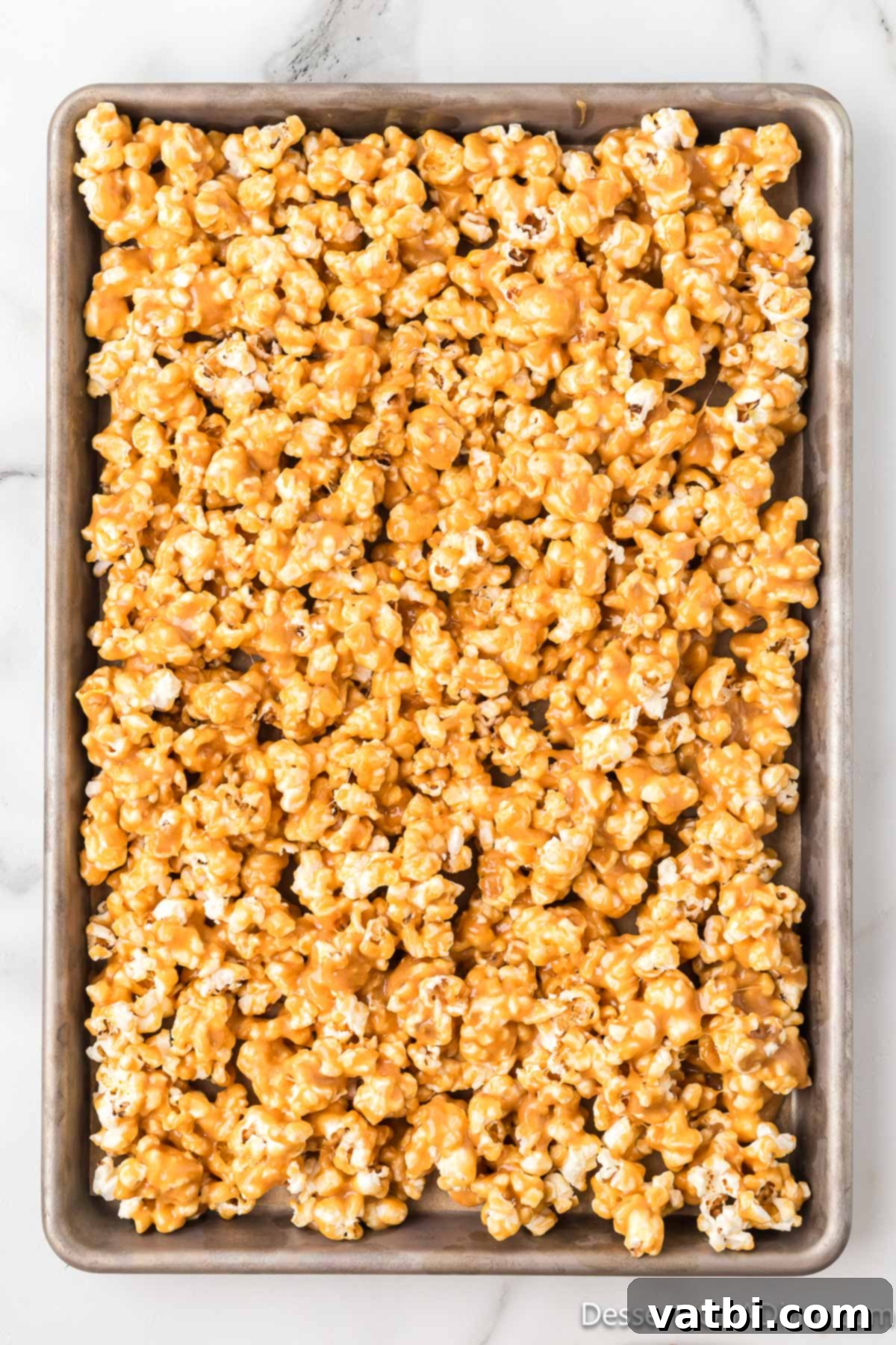 Coated peanut butter popcorn spread out on a baking sheet lined with parchment paper to cool.