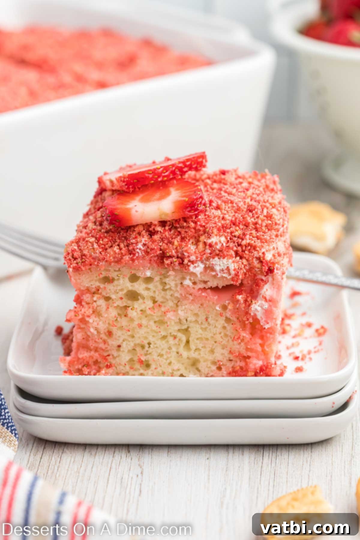 Strawberry Crunch Poke Cake 2 Strawberry Crunch Poke Cake on a white plate, showcasing its layers and crunchy topping