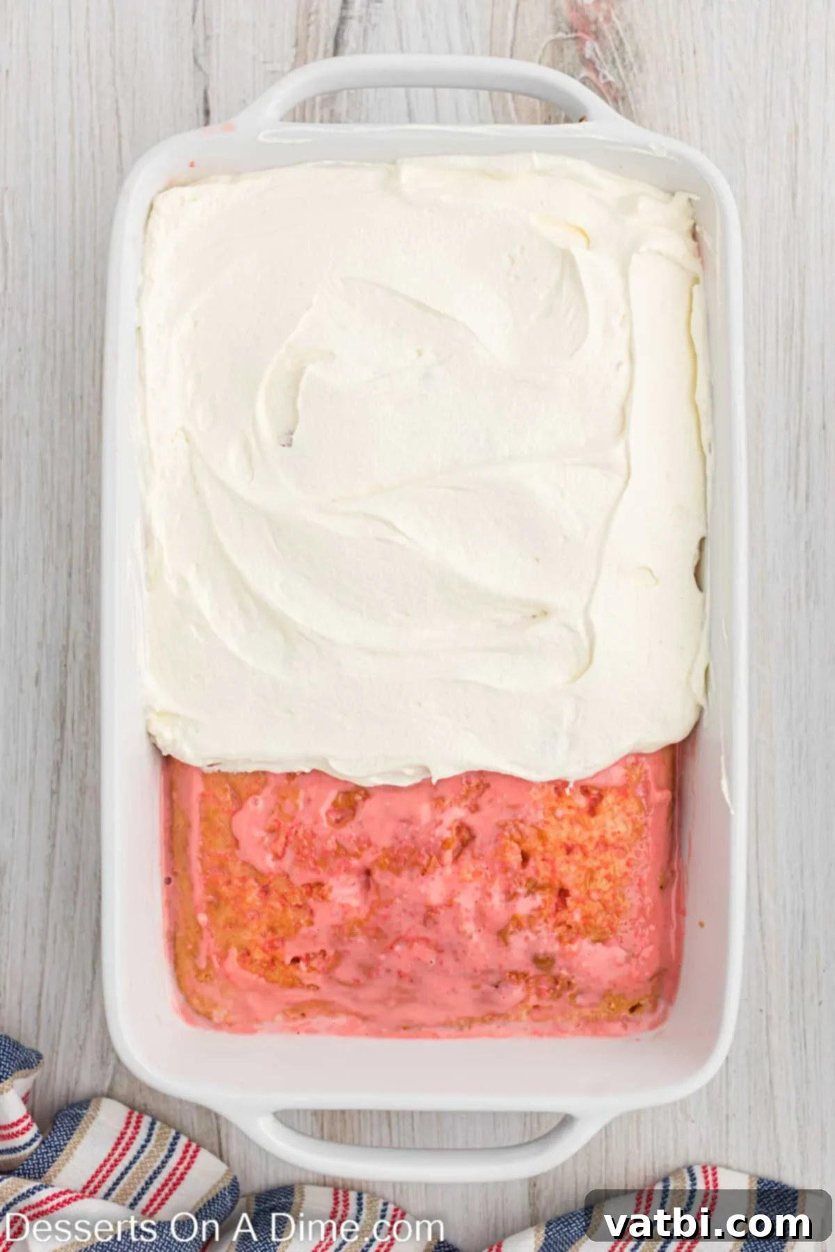 Strawberry Crunch Poke Cake 6 Whipped topping being spread evenly onto the poked cake.