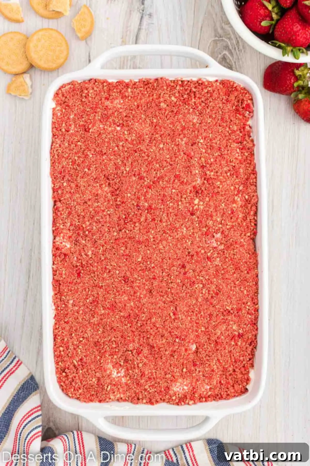 Strawberry Crunch Poke Cake 9 Crunch topping being spread over the whipped cream layer on the cake.