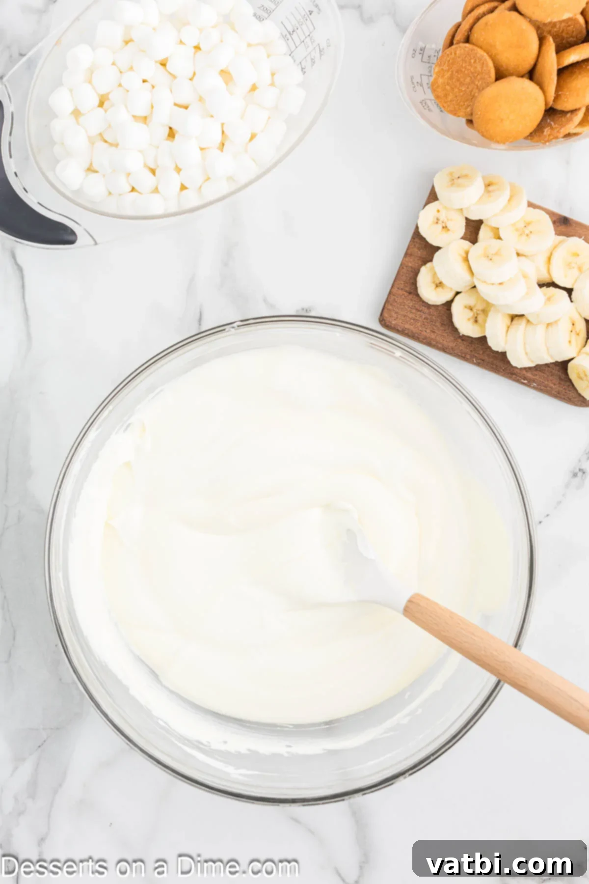 Whipped Banana Bliss 5 Cool Whip being gently folded into the thickened banana pudding mixture in a bowl with a spatula, creating a light, fluffy consistency.