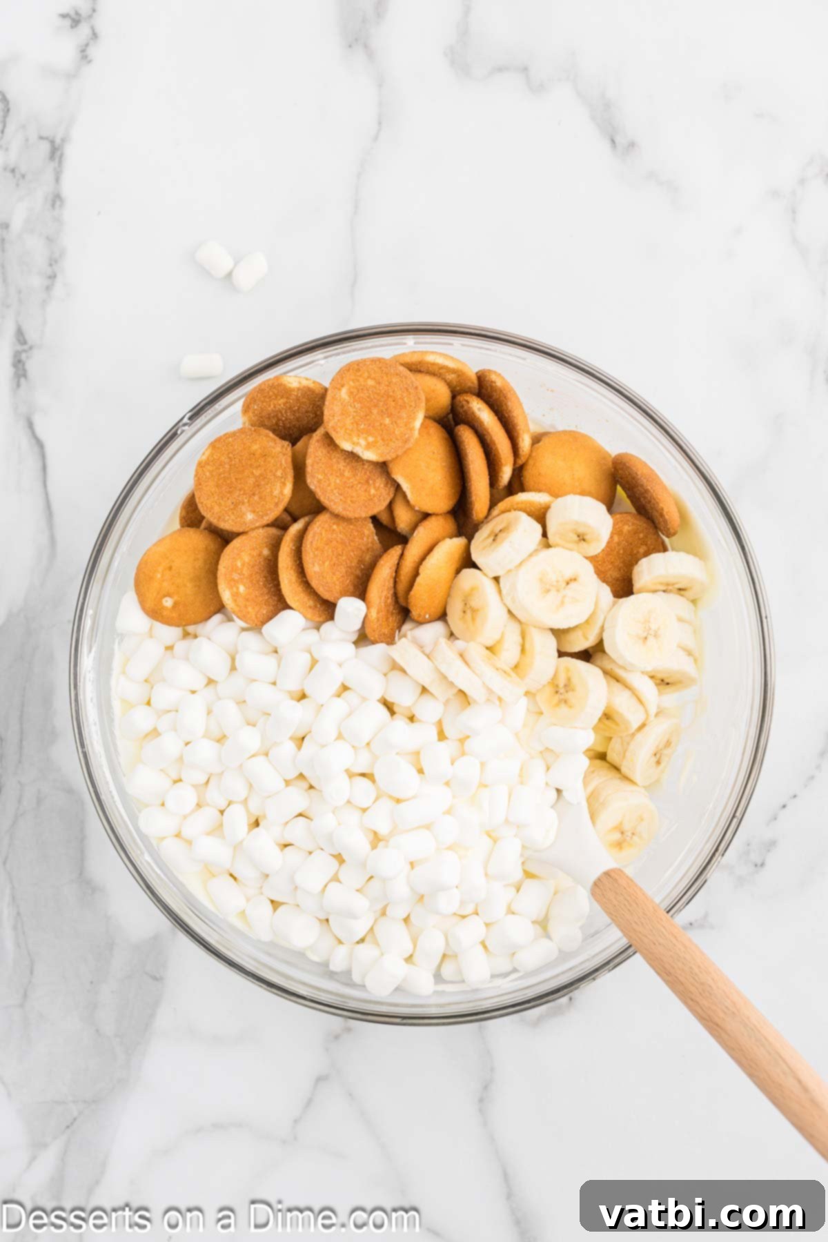 Whipped Banana Bliss 6 A bowl containing the banana pudding and Cool Whip mixture, with mini marshmallows, crushed vanilla wafers, and sliced fresh bananas added on top, ready to be folded in.