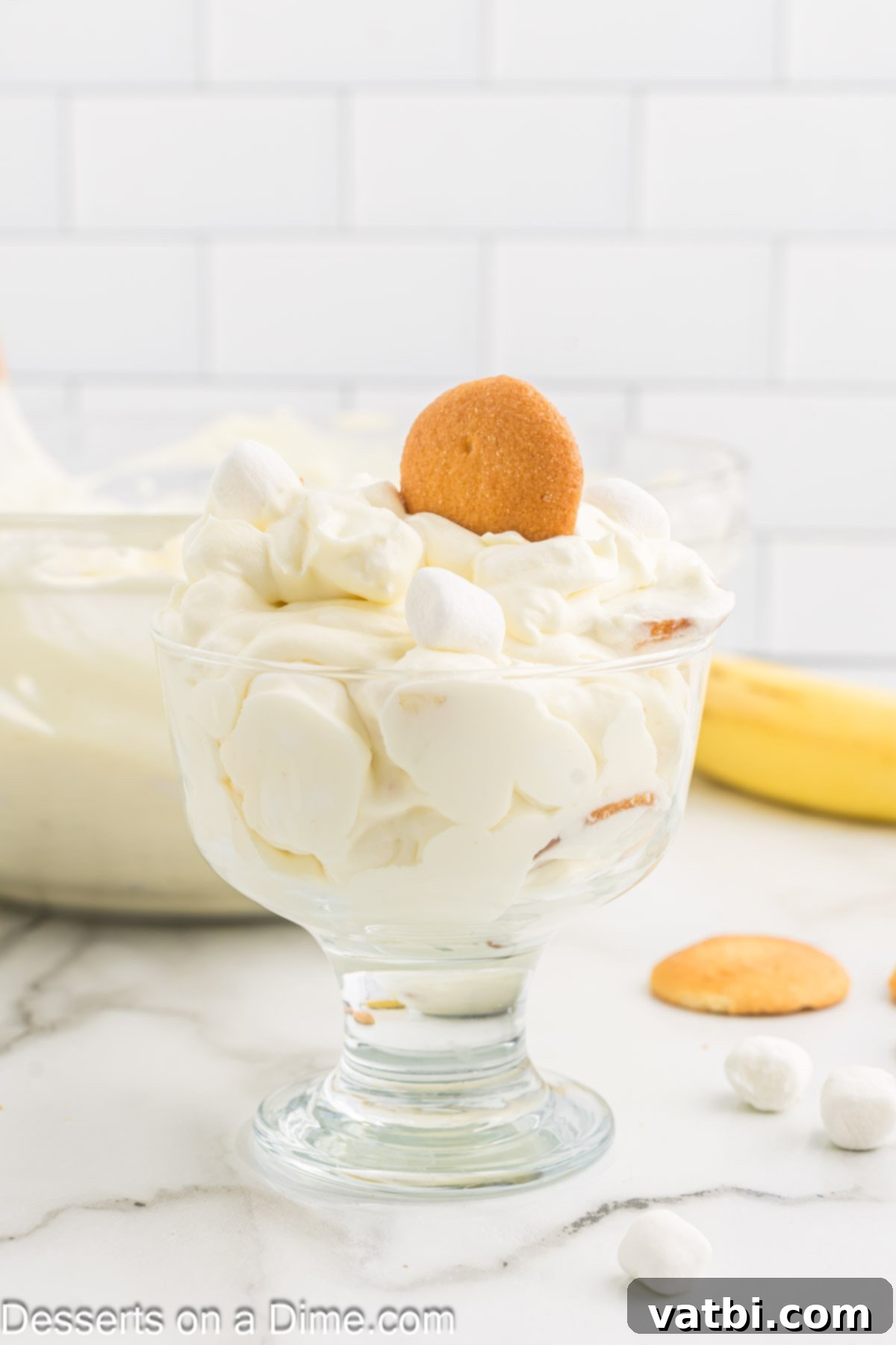 Whipped Banana Bliss 8 A clear glass dish filled with fluffy banana pudding, garnished with a single banana slice and a sprinkle of vanilla wafer crumbs.