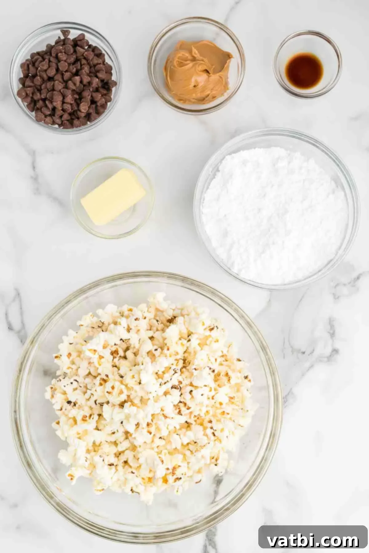 Muddy Buddies Popcorn 3 A collection of ingredients for Puppy Chow Popcorn: fresh popped popcorn, chocolate chips, creamy peanut butter, butter, vanilla extract, and a mound of powdered sugar.