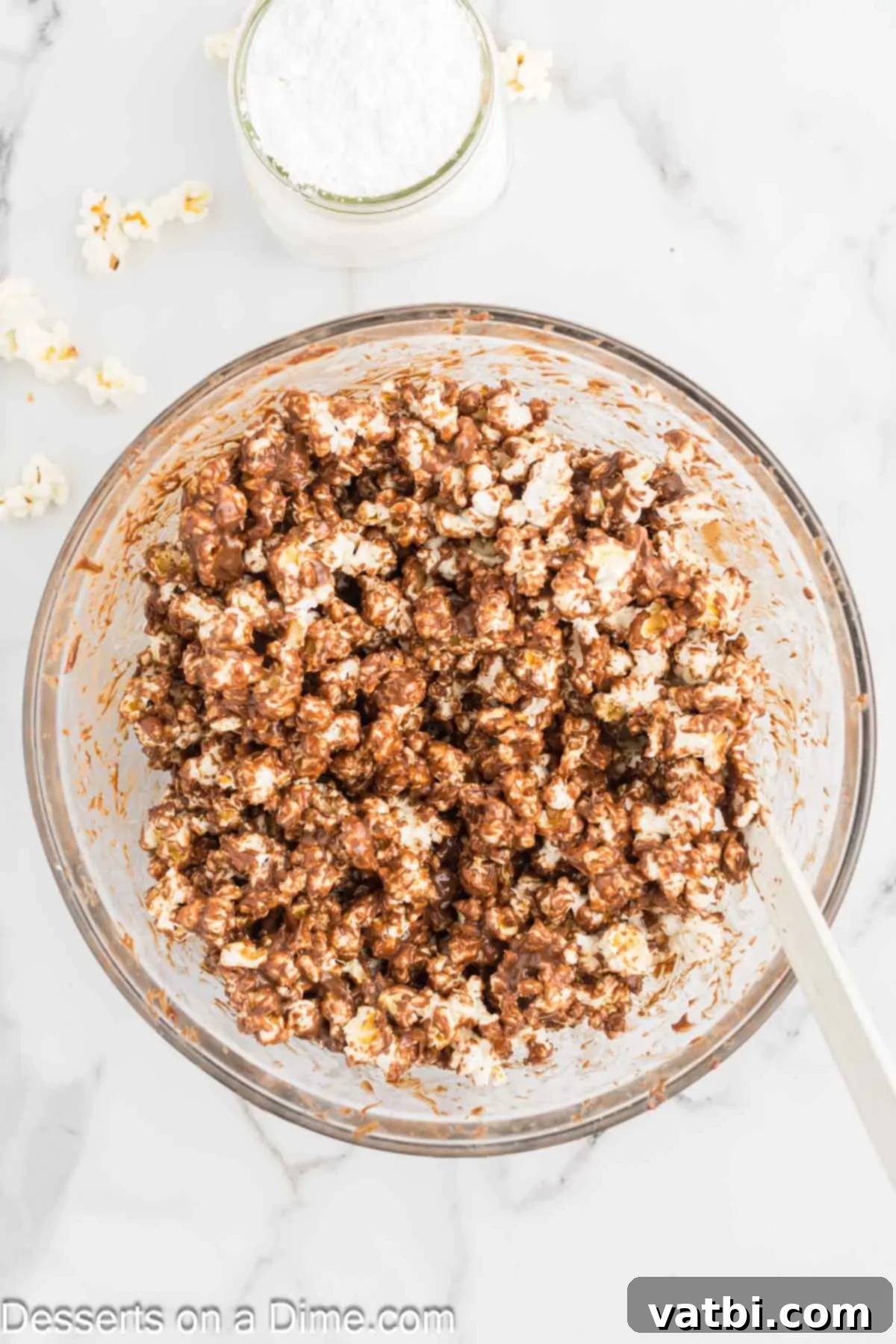 Muddy Buddies Popcorn 5 Warm chocolate and peanut butter coating being poured evenly over a bowl of popcorn.