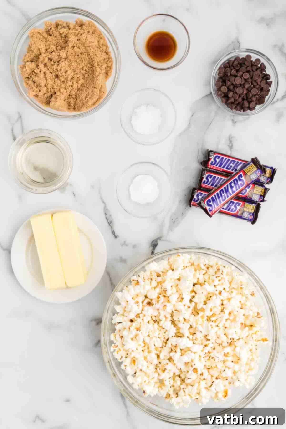 Snickers Popcorn Crunch 3 A flat lay of all the ingredients needed to make Snickers popcorn: popped popcorn, butter, brown sugar, baking soda, vanilla extract, Snickers bars, and semi-sweet chocolate chips.