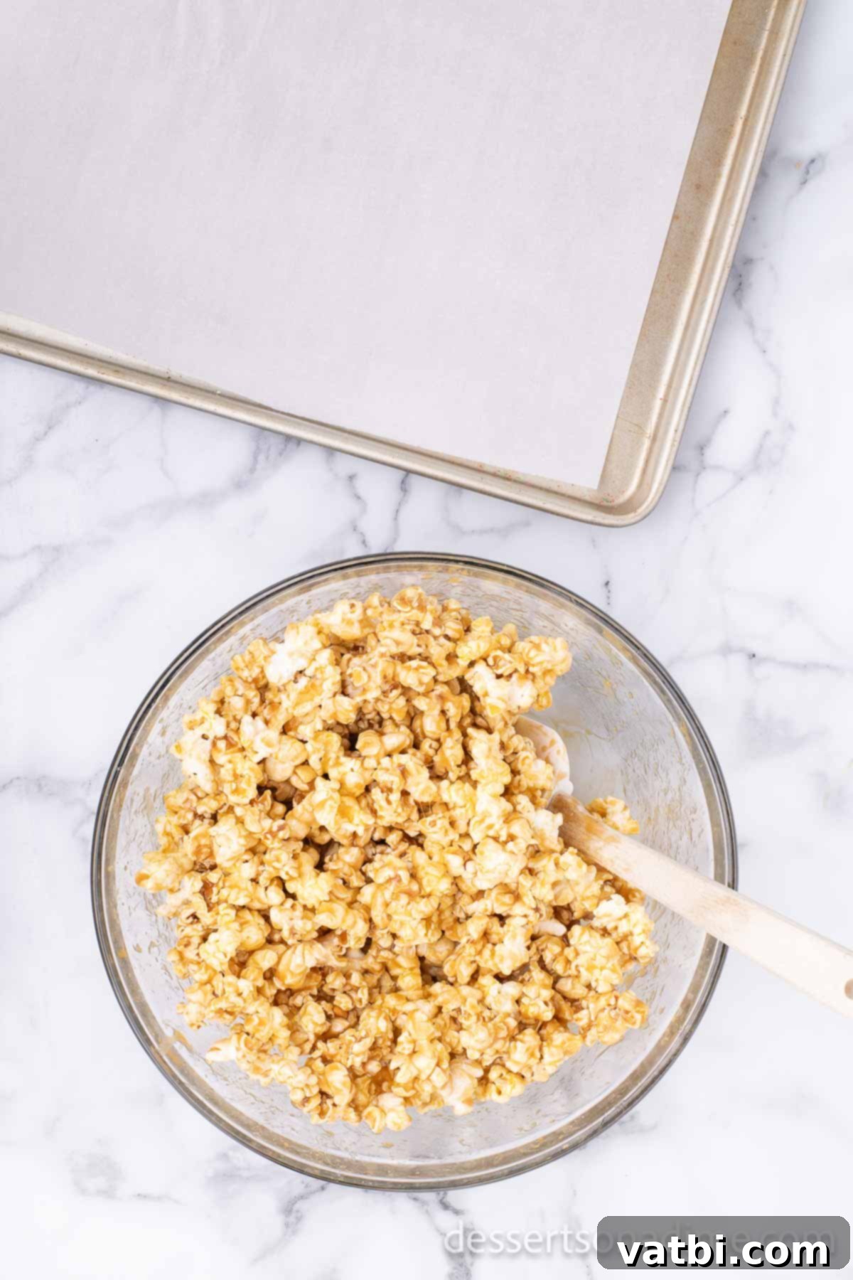 Snickers Popcorn Crunch 5 Popcorn being coated with hot caramel sauce in a large bowl, demonstrating even distribution.
