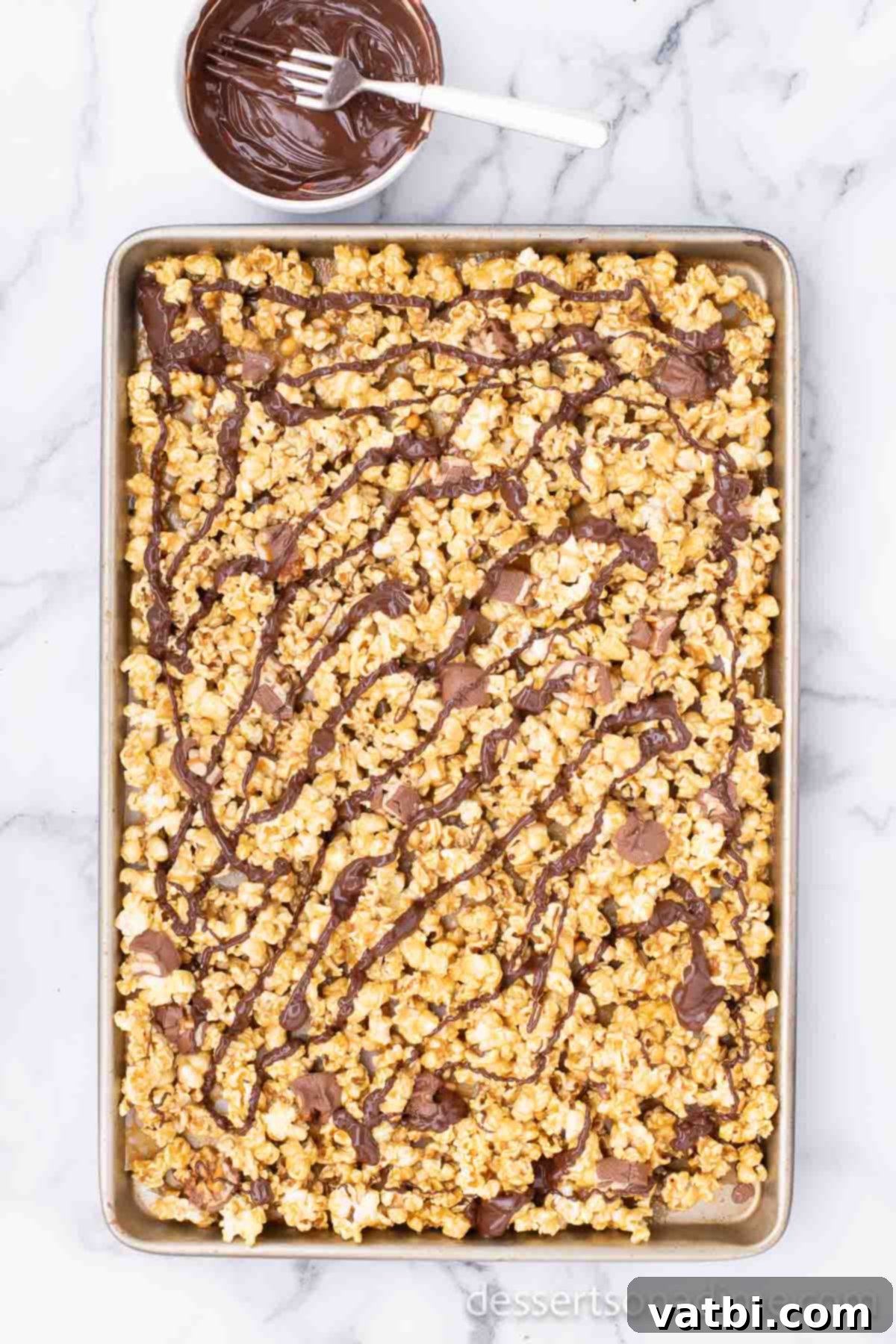 Snickers Popcorn Crunch 8 Melted semi-sweet chocolate being drizzled in thin lines over the cooling Snickers popcorn.