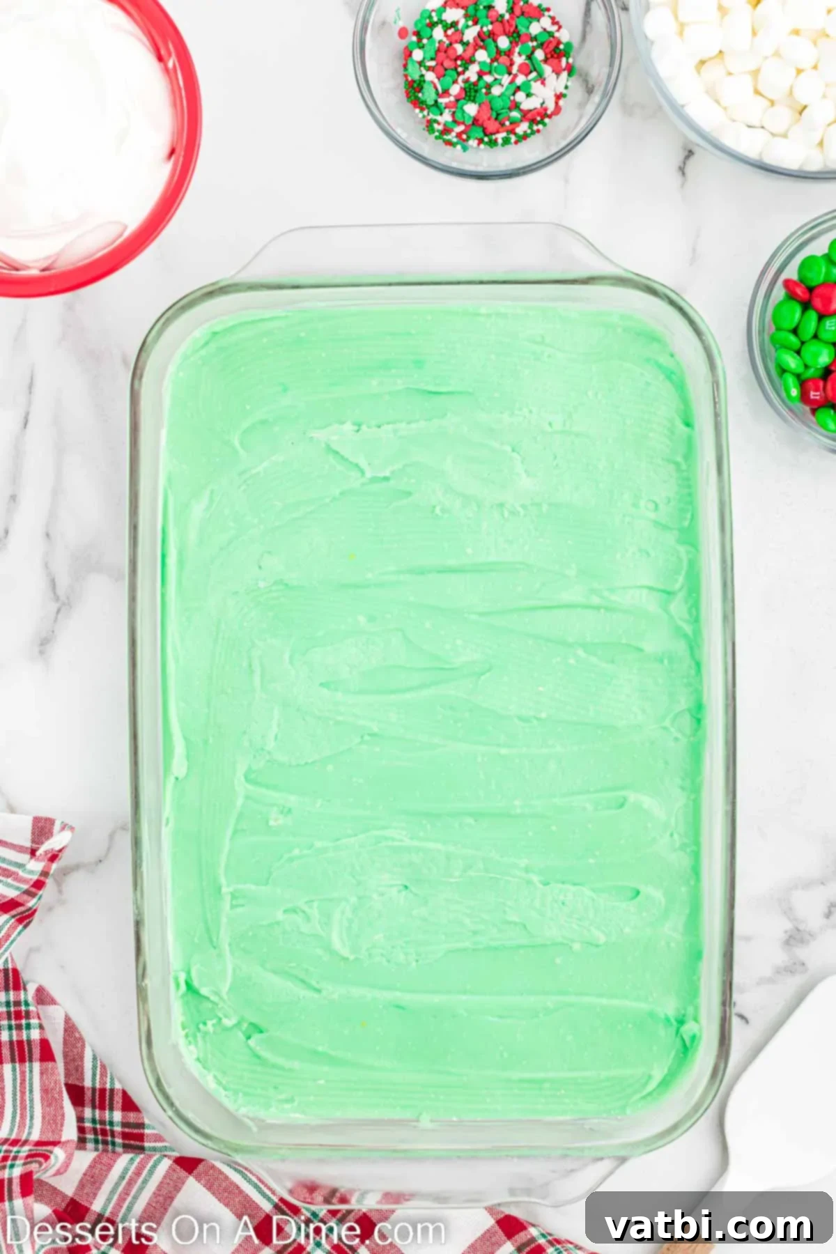 Christmas Layered Dream Dessert 7 The vibrant green pudding layer being spread smoothly over the white peppermint cheesecake layer in the baking pan.