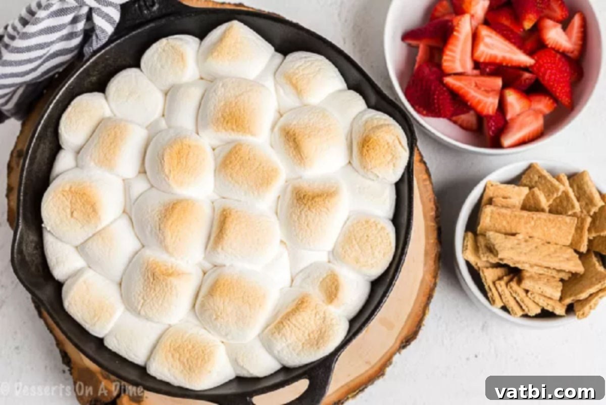 With only 2 ingredients needed, S'mores dip is the perfect treat to enjoy any day of the week. We love to make this dip for parties, snacks or just because. Smores dip in a cast iron skillet with a side of strawberries and graham crackers for dipping