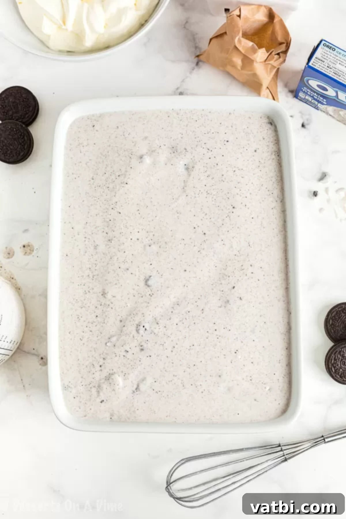 Ultimate Oreo Poke Cake 3 The creamy Oreo pudding mixture evenly spread across the surface of the poke cake, ensuring all holes are filled and the cake is fully covered.