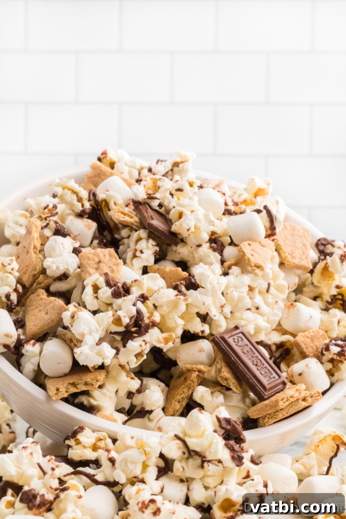 A bowl filled with homemade S'mores Popcorn, featuring fluffy popcorn, melted chocolate, mini marshmallows, and graham cracker pieces.