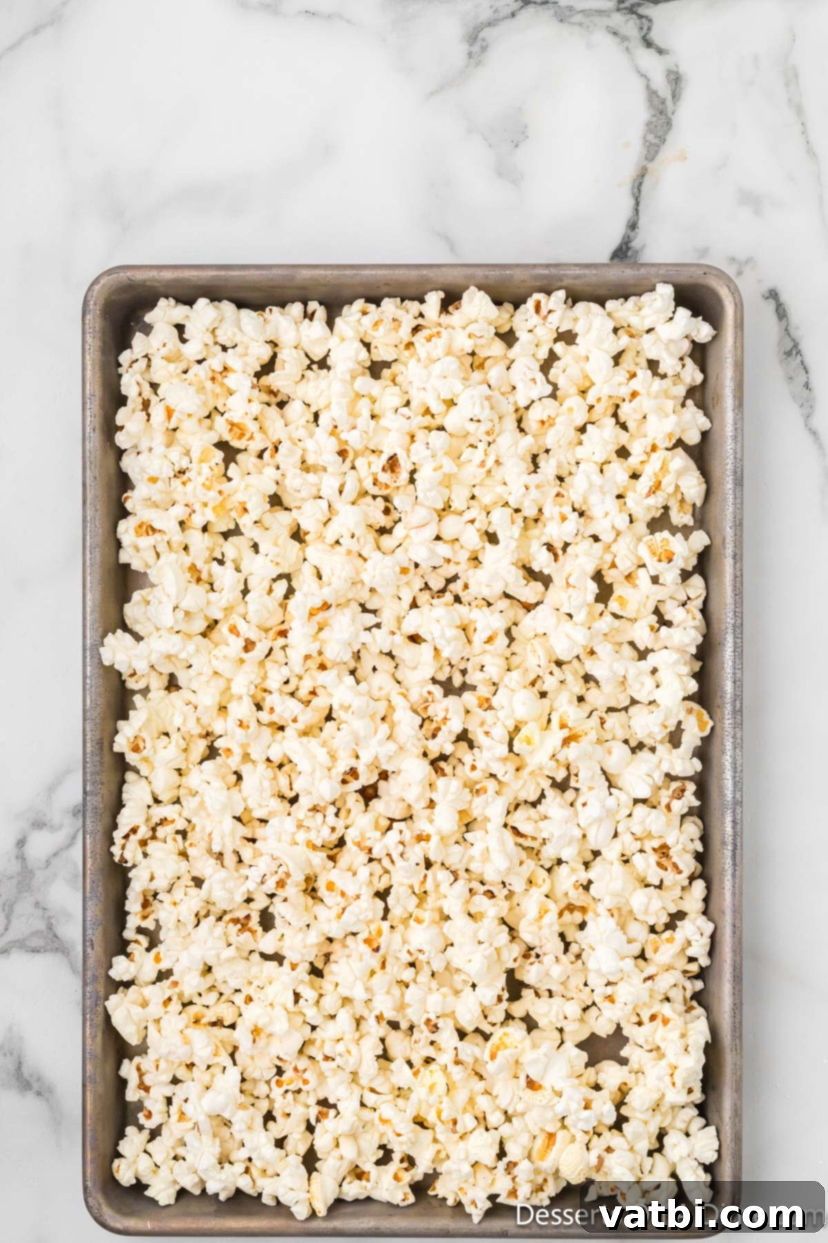 Freshly popped popcorn spread out on baking sheets lined with parchment paper, ready for toppings.