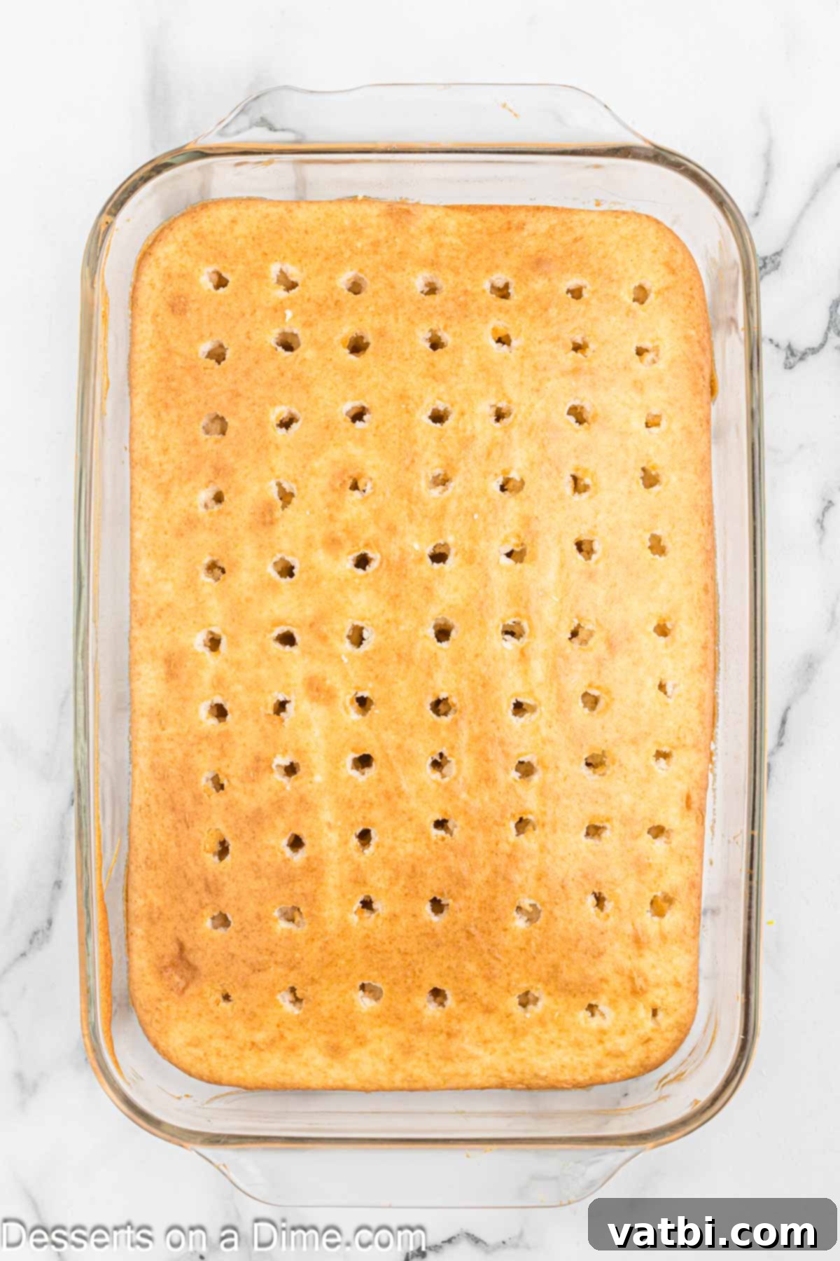 Festive Christmas Jello Poke Cake 5 A baked cake with numerous holes poked into its surface using the handle of a wooden spoon.