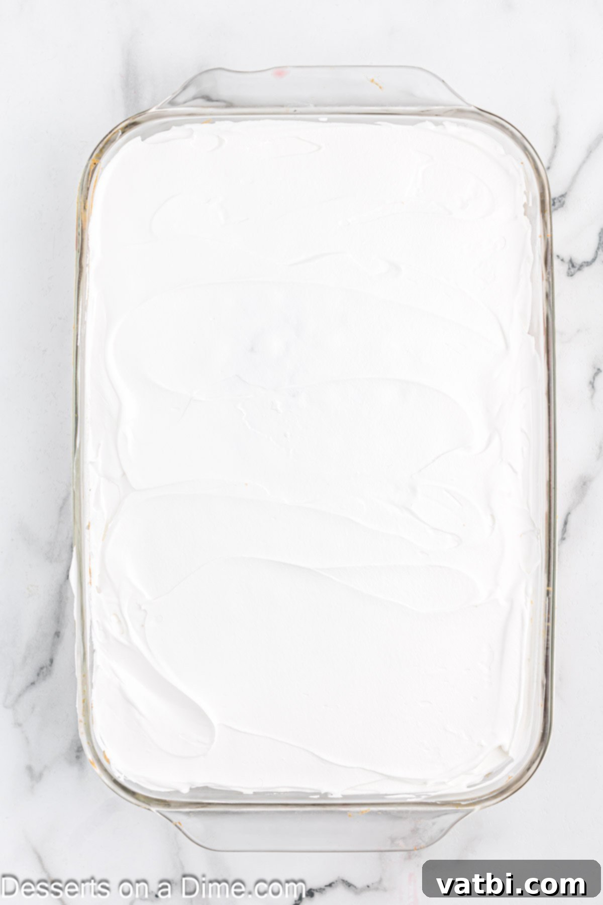 Festive Christmas Jello Poke Cake 8 A cake covered with a smooth layer of white whipped cream, ready for sprinkles.