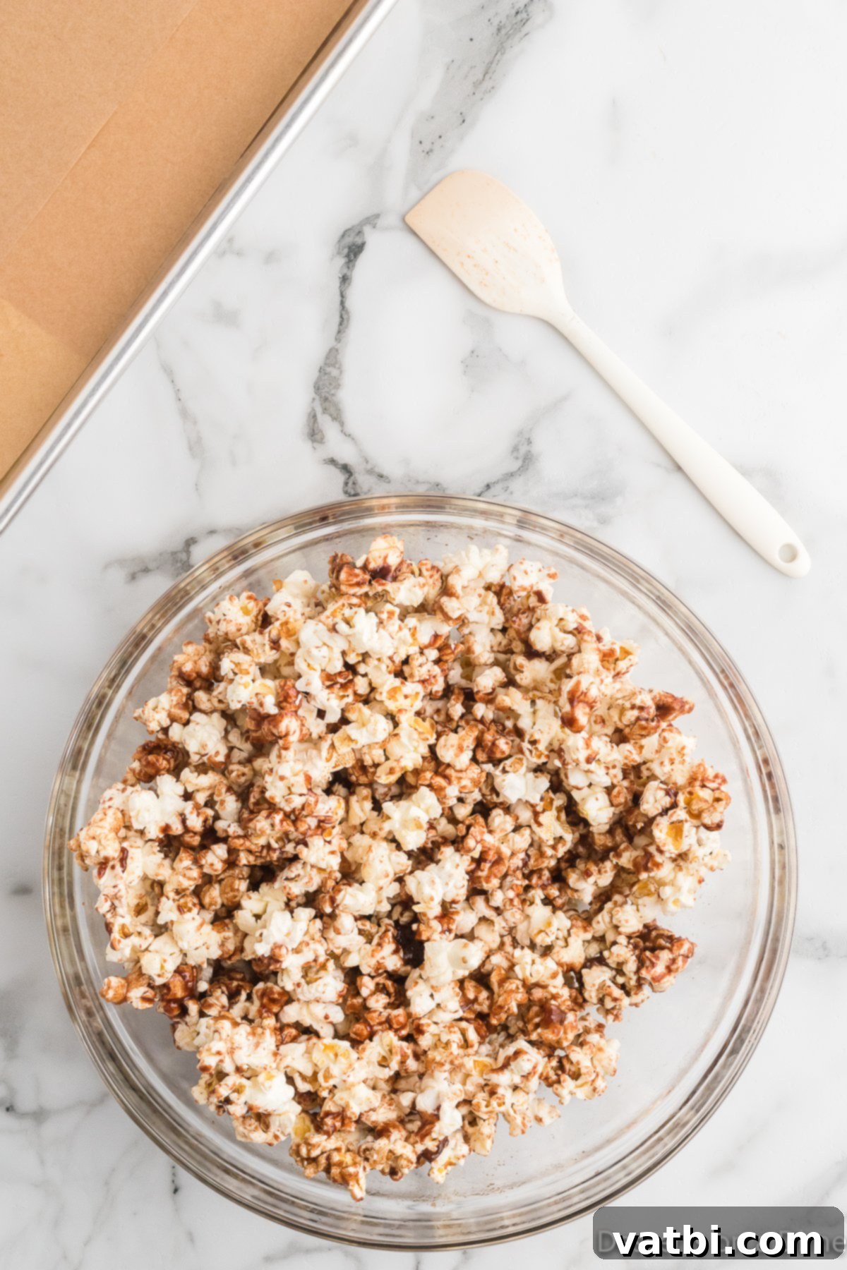 Irresistible Cinnamon Sugar Popcorn 7 Warm cinnamon sugar mixture being poured over a large bowl of fluffy popcorn.