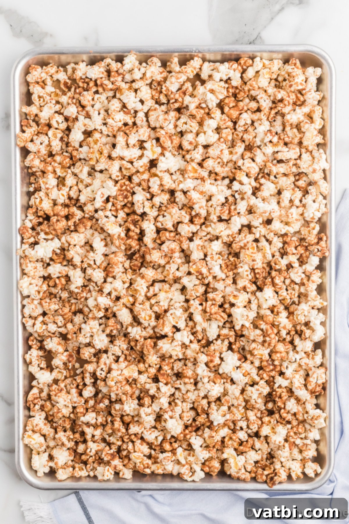 Irresistible Cinnamon Sugar Popcorn 8 Cinnamon sugar coated popcorn spread evenly on a parchment-lined baking sheet.