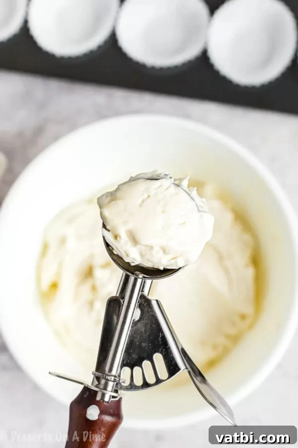 Decadent Keto Cheesecake Fat Bombs 3 Scooping creamy Keto Cheesecake Fat Bomb batter with a cookie scoop into a mini cupcake liner.