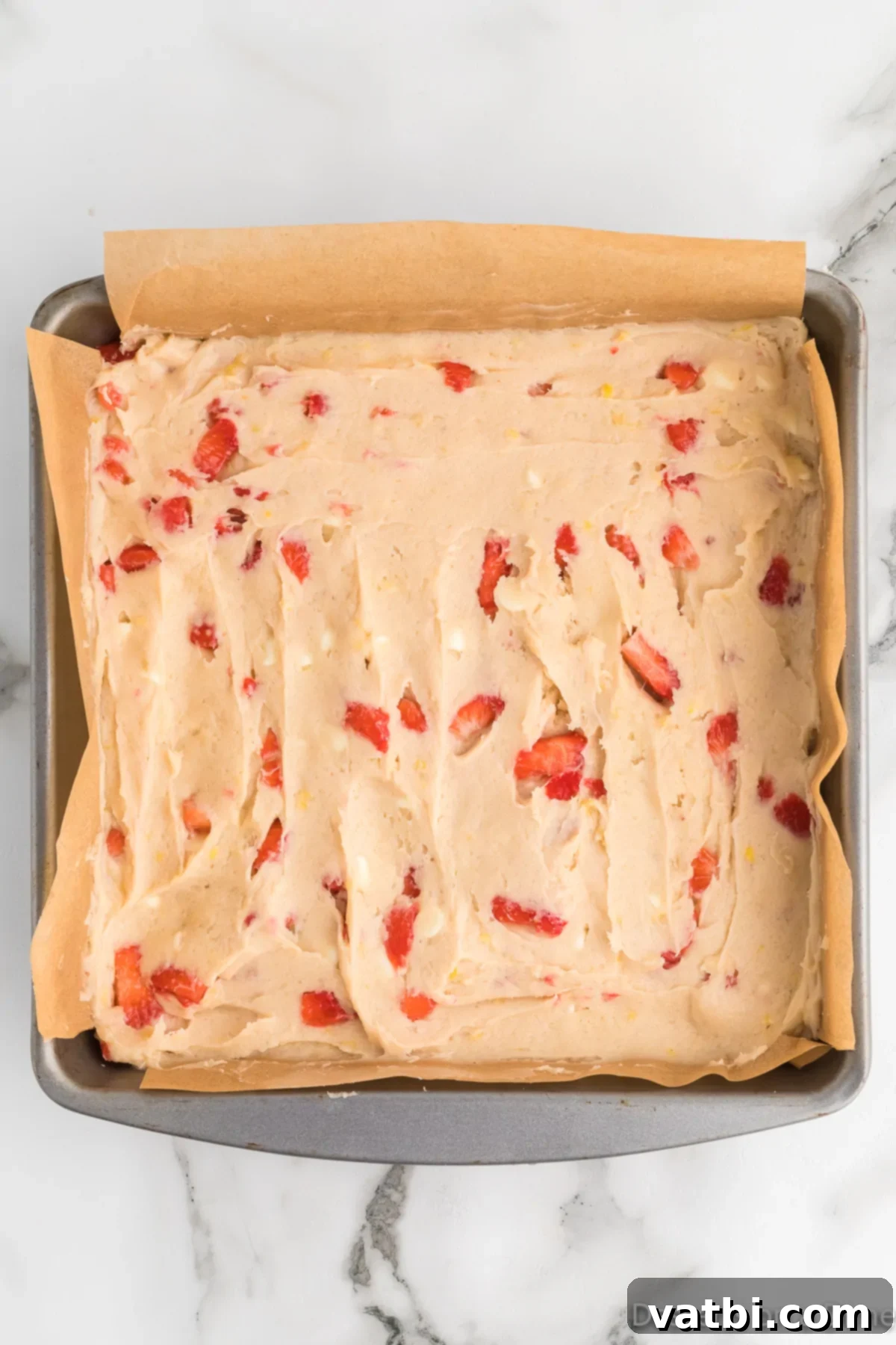 Zesty Strawberry Lemon Blondie Delight 9 Blondie batter spread evenly in a parchment-lined baking pan, ready for the oven.