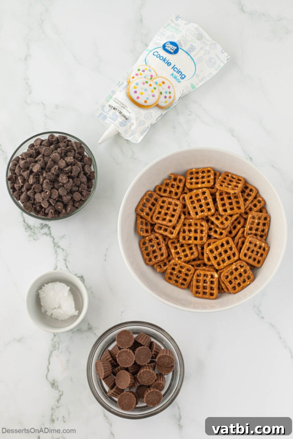 All the essential ingredients laid out: crunchy pretzels, mini Reese's peanut butter cups, semi-sweet chocolate chips, and white decorating icing.