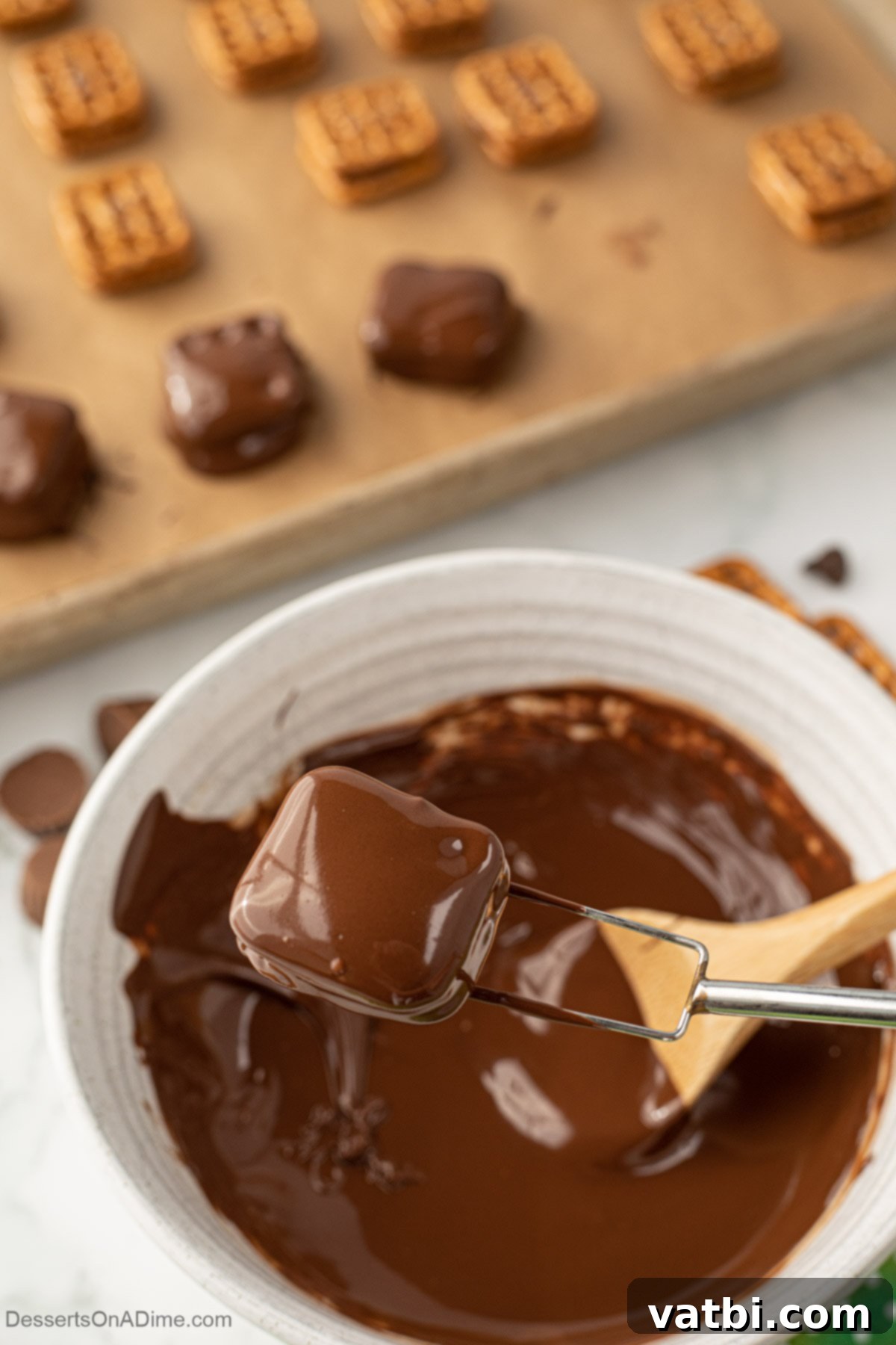 A pretzel sandwich being carefully dipped into the melted chocolate, ready to be fully coated.