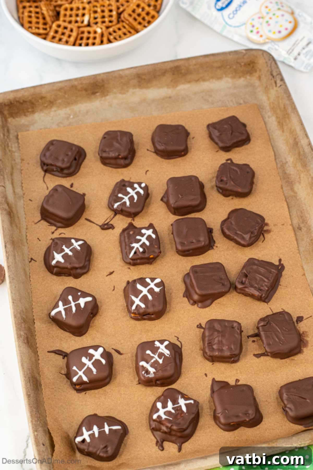 Freshly chocolate-dipped pretzel cookies cooling on a baking sheet lined with parchment paper.