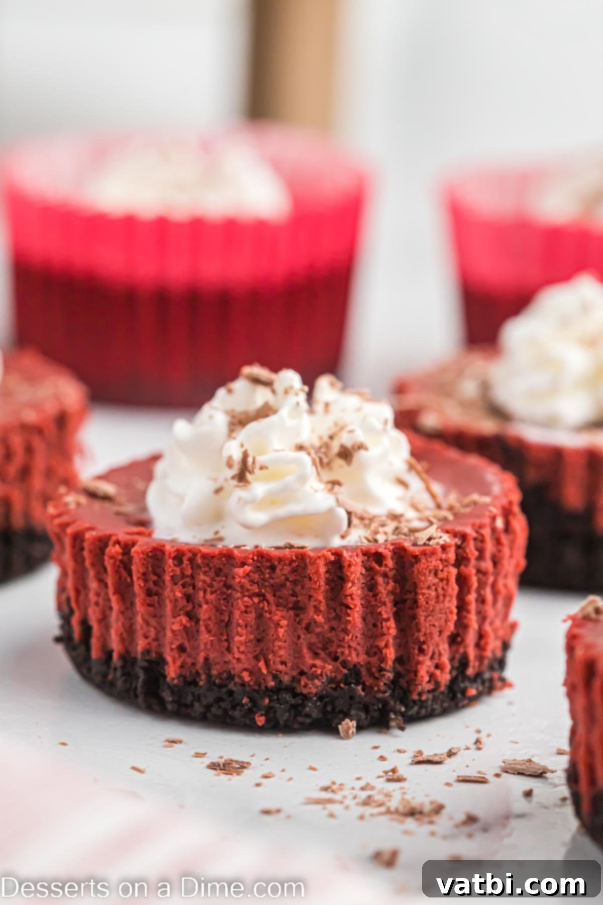 Mini red velvet cheesecake ready to serve, adorned with whipped cream and chocolate shavings.