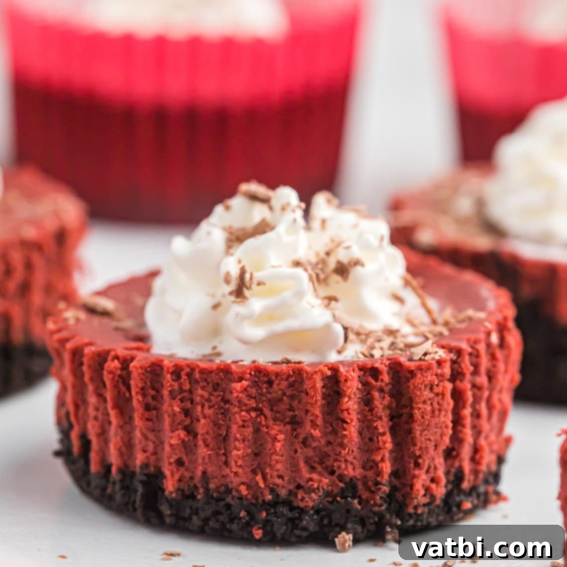 Mini red velvet cheesecake garnished with whipped cream and chocolate, ready for a dessert table.
