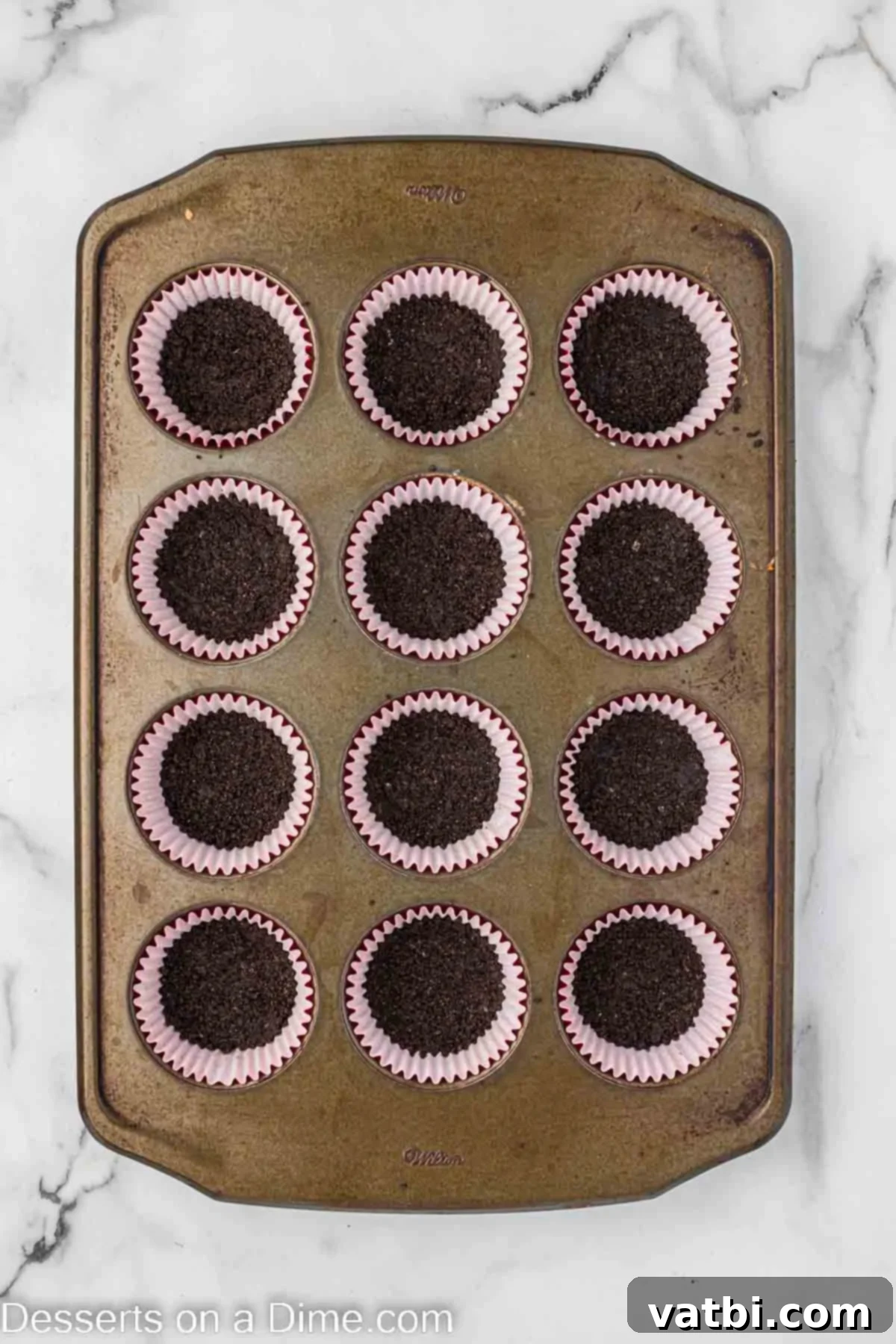 Crushed Oreo cookies and butter mixture pressed into muffin cups, forming the crust.