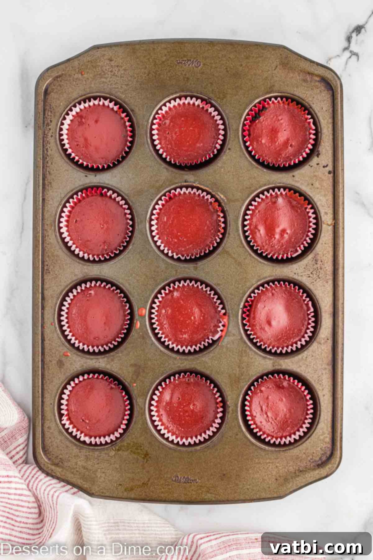 Red velvet cheesecake batter poured into muffin tins on top of the cookie crusts.
