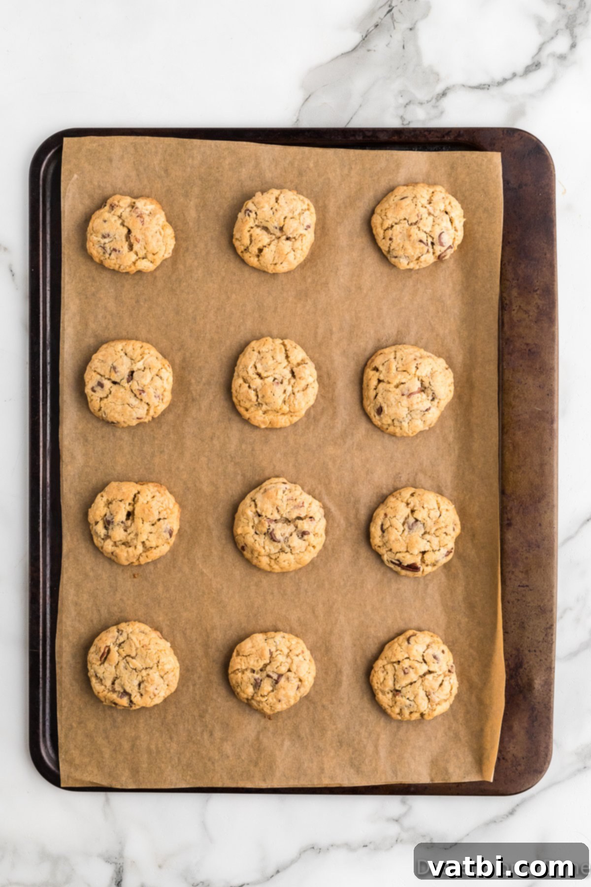Loaded Cowboy Cookies 10 Freshly baked Cowboy cookies cooling on a baking sheet, with lightly browned edges.