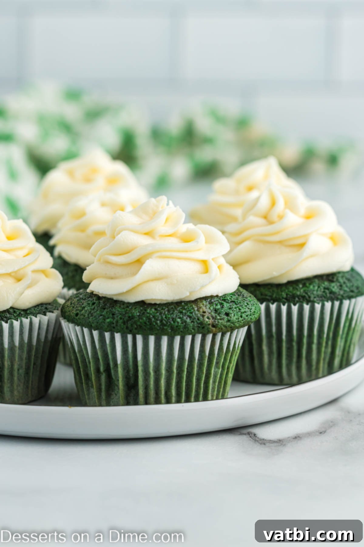 Lush Green Velvet Cupcakes 15 A delightful arrangement of green velvet cupcakes, each topped with a generous swirl of cream cheese frosting, presented on a white serving platter.