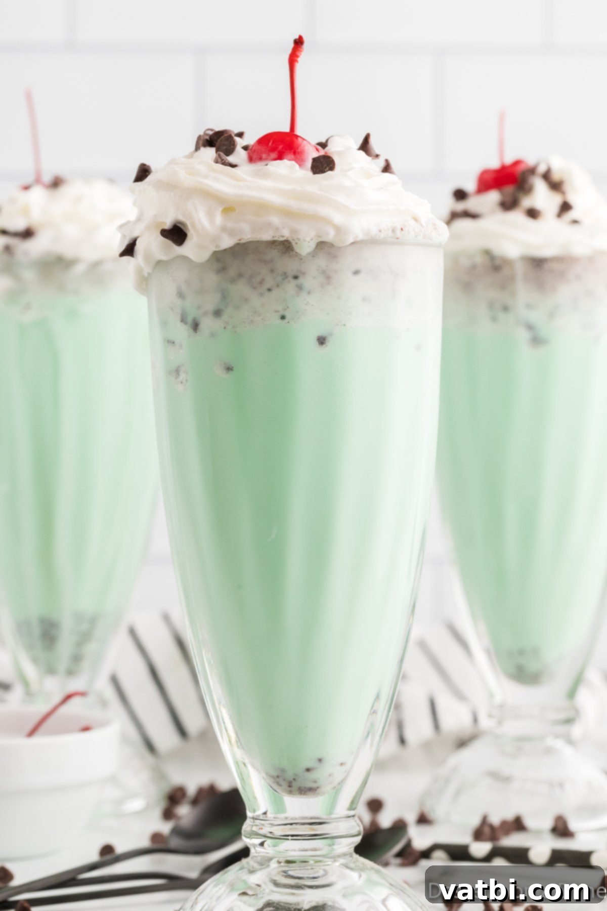 Ultimate Mint Chocolate Chip Milkshake 2 Glasses of mint chocolate chip milkshakes, garnished with whipped cream, chocolate chips, and a cherry.