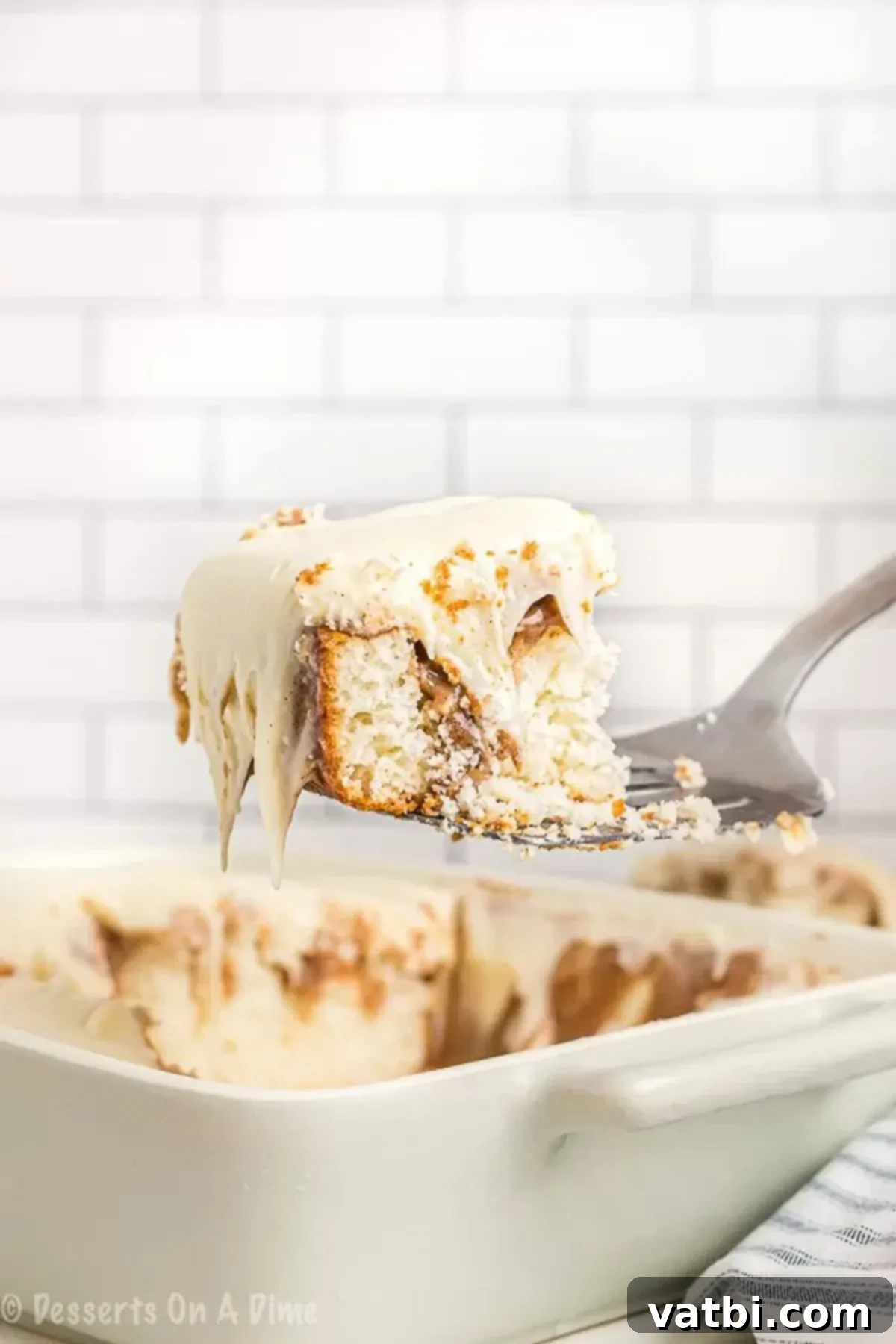 Cinnamon Roll Poke Cake Recipe is a yummy cake with lots of cinnamon and cream cheese icing. Enjoy everything you love about cinnamon rolls in an easy cake. A glorious slice of Cinnamon Roll Poke Cake, showcasing its moist layers, cinnamon swirl, and thick cream cheese frosting, served on a spatula.