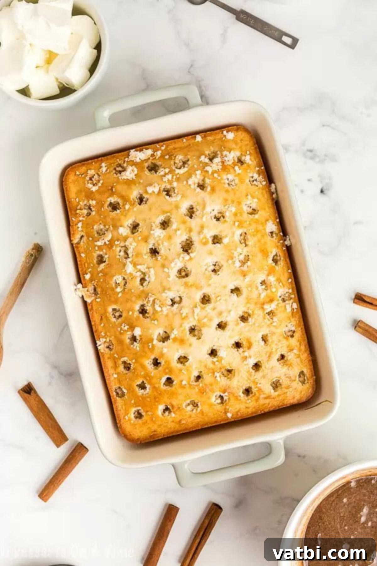 Irresistible Cinnamon Roll Poke Cake 3 A freshly baked cake with numerous holes poked evenly across its surface, ready to absorb the delicious cinnamon filling.