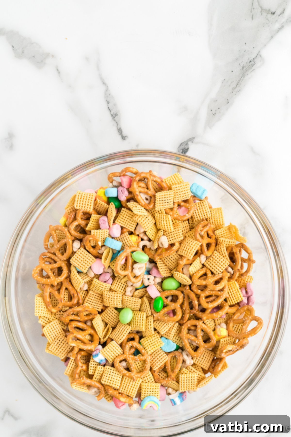 Emerald Enticement 4 Large bowl filled with a dry mixture of Chex cereal, Lucky Charms, mini pretzels, and green M&Ms, ready for the chocolate coating.